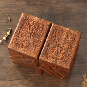 May include: Two wooden boxes with intricate floral carvings. The boxes are a warm brown color and appear to be made of wood. The floral design is carved into the top and sides of the boxes, adding a decorative element. The boxes are closed and appear to be hinged.
