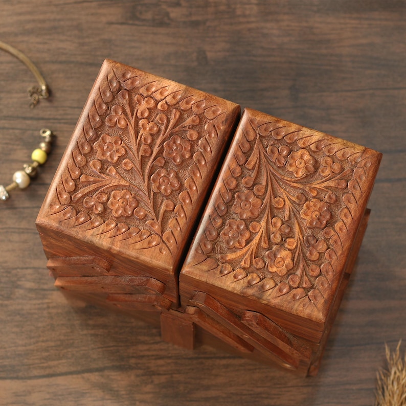 May include: Two wooden boxes with intricate floral carvings. The boxes are a warm brown color and appear to be made of wood. The floral design is carved into the top and sides of the boxes, adding a decorative element. The boxes are closed and appear to be hinged.