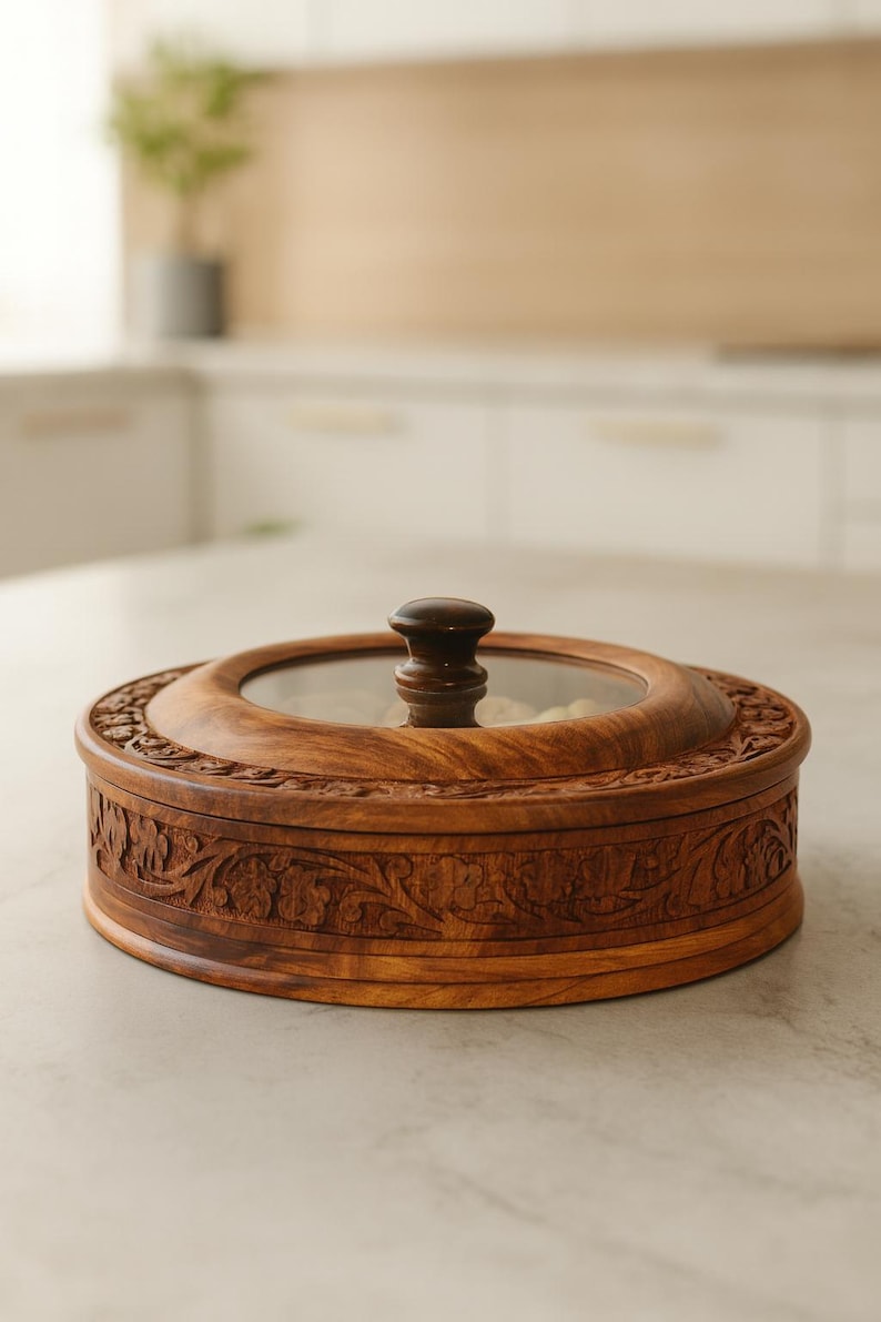 May include: A circular wooden serving dish with a glass lid and a dark brown handle. The dish has detailed floral carvings around the edge. The wooden dish is on a light-coloured countertop.