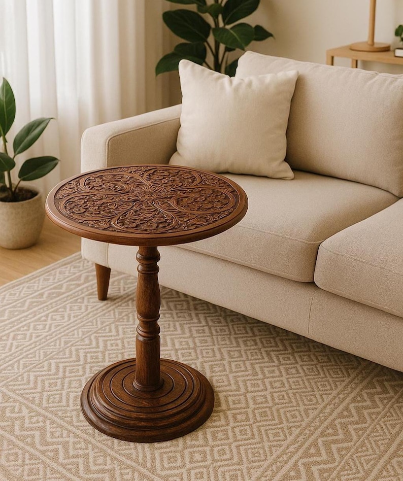 May include: A round, dark brown wooden side table with intricate floral carvings on the tabletop. The table has a single, turned pedestal base and a circular foot. The table is approximately 24 inches tall and 20 inches in diameter.