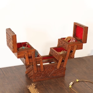 May include: A wooden jewelry box with multiple compartments, carved with floral patterns. The interior is lined with red fabric. The box is open, displaying various pieces of jewelry, including necklaces and bracelets. The box is on a wooden surface.