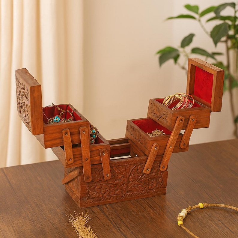May include: A wooden jewelry box with multiple compartments, lined with red velvet. The box is intricately carved with floral patterns and contains various pieces of jewelry, including necklaces and bracelets.