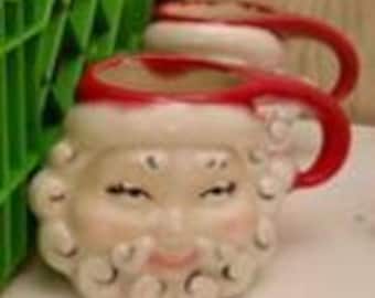 Puede incluir: Dos tazas de cerámica vintage de Papá Noel con asas rojas y ribetes blancos y rojos. Las tazas presentan una cara sonriente de Papá Noel con barba blanca y mejillas sonrosadas.