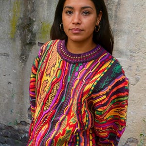 Frau trägt farbenfrohen Vintage-Pullover mit 90er-Jahre-Muster – Oversized, handgestrickter Retro-Strickpullover in leuchtenden Farben wie Rot, Lila, Gelb und Grün. Boho-Streetstyle und Unikat im Coogi-Stil, ideal für Mode-Liebhaberinnen, Festival-Outfits oder kreative Wintermode. Ethno-inspirierter Look, perfekt für Individualistinnen.