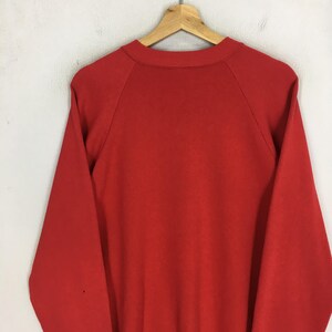 May include: A solid red sweatshirt with long sleeves, hanging on a wooden hanger. The raglan sleeves extend from the neckline to the underarm. The sweatshirt is made of a soft material.