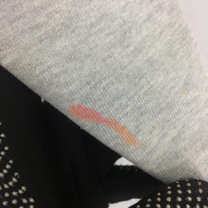 May include: Close-up of a gray sweatshirt sleeve with a pink and orange stain. The sleeve is folded over a black fabric with white polka dots. The fabric is a soft, knit material.