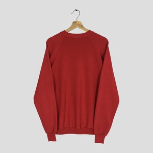 May include: A solid red sweatshirt with long sleeves, raglan sleeves, and a crew neck, hanging on a wooden hanger. The sweatshirt is made of a soft material and is a classic style.