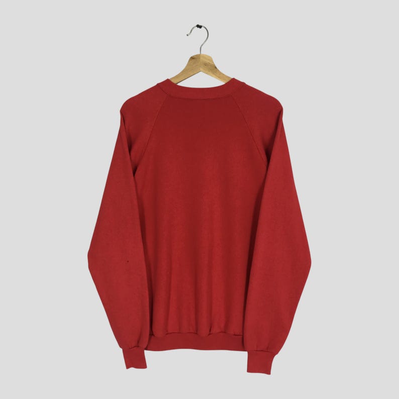 May include: A solid red sweatshirt with long sleeves, raglan sleeves, and a crew neck, hanging on a wooden hanger. The sweatshirt is made of a soft material and is a classic style.