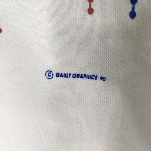 May include: Close-up of a white fabric with a pattern of red and blue dots. The text "&copy; GAULT GRAPHICS 90" is printed in blue. The fabric has a textured appearance.