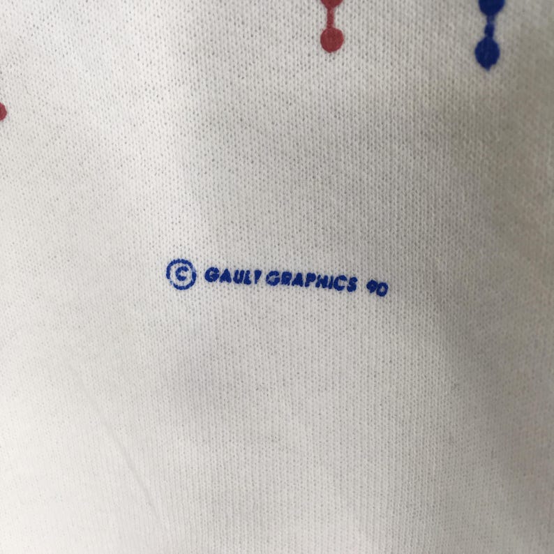 May include: Close-up of a white fabric with a pattern of red and blue dots. The text "&copy; GAULT GRAPHICS 90" is printed in blue. The fabric has a textured appearance.