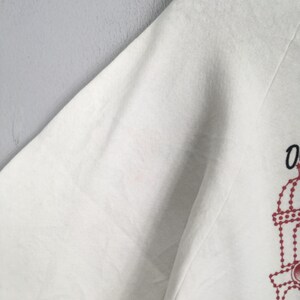 May include: White long-sleeved sweatshirt with a red and black graphic design on the lower right side. The design appears to be a stylized illustration. The sweatshirt is made of a soft, comfortable material.