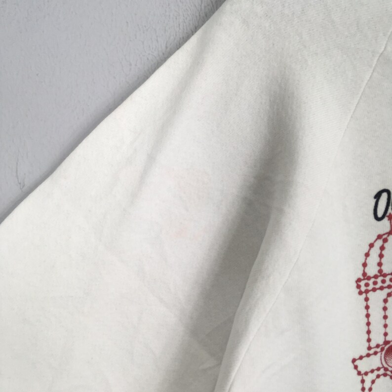 May include: White long-sleeved sweatshirt with a red and black graphic design on the lower right side. The design appears to be a stylized illustration. The sweatshirt is made of a soft, comfortable material.