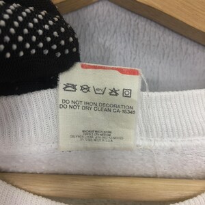 May include: Close-up of a white fabric tag with care instructions. The tag includes symbols for washing, drying, and ironing, along with text indicating the garment should not be ironed or dry cleaned. The tag also has the text "CA-18345".