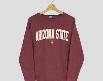 May include: Maroon crewneck sweatshirt with the text "ARIZONA STATE" in white arched lettering. A small gold-colored emblem is centered below the text. The sweatshirt is hanging on a wooden hanger.