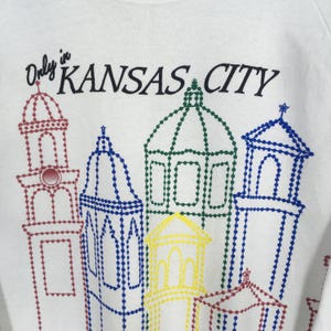 May include: White sweatshirt featuring the text "Only in KANSAS CITY" above a colorful dotted outline of city buildings. The buildings are outlined in red, blue, green, and yellow.