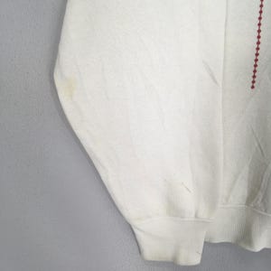 May include: Off-white sweatshirt with a crew neck and long sleeves. The sleeve cuff is ribbed. A vertical line of small red dots is on the right side of the sweatshirt. There are some stains on the left sleeve.