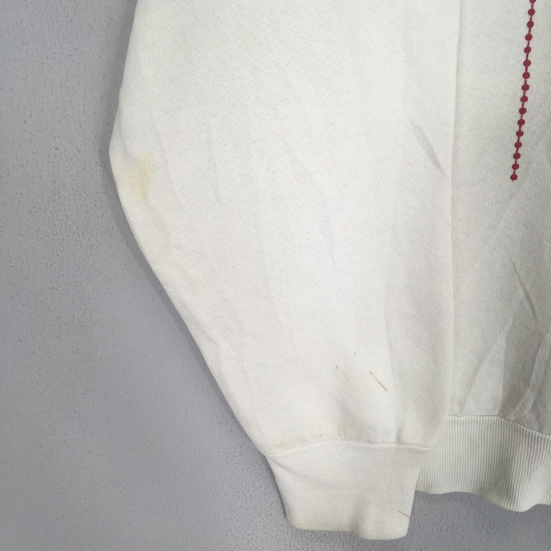 May include: Off-white sweatshirt with a crew neck and long sleeves. The sleeve cuff is ribbed. A vertical line of small red dots is on the right side of the sweatshirt. There are some stains on the left sleeve.