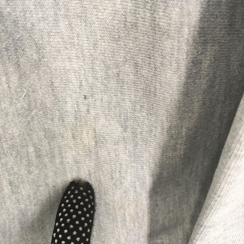 May include: Close-up of a light gray fabric with a textured surface. The fabric has a few small dark spots and a lighter area. A black and white polka-dotted object is in the foreground.