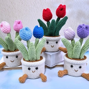 May include: Five crocheted potted plants with smiling faces. Each pot has a different color flower, including pink, blue, purple, and red.