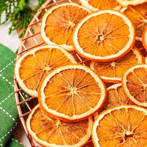 May include: Close-up of dried orange slices arranged on a copper-colored wire rack. The orange slices are a warm, golden-brown color, with visible textures and patterns. The image suggests a theme of food, possibly for decoration or culinary use.