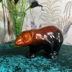 以下が含まれることがあります： 光沢仕上げのセラミック製のクマの置物。クマは茶色の頭と黒い体を持っています。この置物は、棚やテーブルに飾るための装飾品です。
