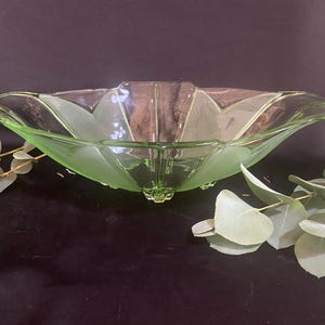 Può includere: Una ciotola di vetro verde con un design unico a smerlo. La ciotola ha una forma ampia e aperta con un aspetto smerigliato e strutturato. La ciotola è sostenuta da piccoli piedini e probabilmente viene utilizzata per servire o esporre.