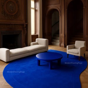 Może przedstawiać: Nowoczesny salon z żywym niebieskim dywanem o organicznym kształcie. Pokój obejmuje beżową sofę, fotel i okrągły niebieski stolik kawowy. Ściany są wyłożone ciemnym drewnem.