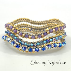 May include: Stack of beaded bracelets in gold, purple, and blue. The bracelets feature intricate beadwork with various sizes and colors of beads. The bracelets are stacked on top of each other. The name "Shelley Nybakke" is written in cursive at the bottom.