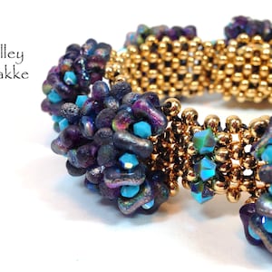 Pode incluir: Um bracelete de contas douradas e roxas com detalhes turquesa. O bracelete é feito com contas pequenas e redondas e tem um design tecido.