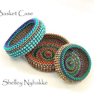 May include: Three beaded items in turquoise, purple, gold, green, and orange. One is a bracelet, and two are circular, possibly coasters or small bowls. The text "Basket Case" and "Shelley Nybakke" are also visible.