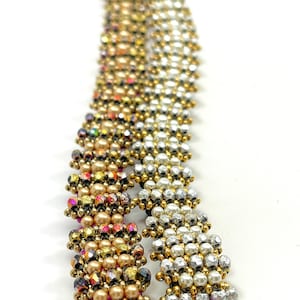 May include: Two beaded bracelets, one with gold and iridescent beads and the other with silver and white beads. Both bracelets feature a geometric pattern.