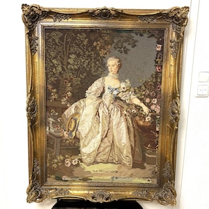 Könnte beinhalten: Gerahmtes Wandteppich, das eine Frau in einem historischen Kleid zeigt, die in einem Garten sitzt. Der Wandteppich hat einen goldenen, verzierten Rahmen. Die Frau ist von Blumen und Laub umgeben, mit detailliertem Hintergrund.