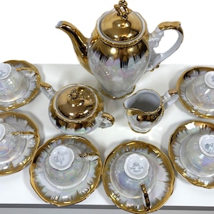 Könnte beinhalten: Ein Vintage-Tee-Set mit goldenen Akzenten und perlmuttartigem Finish. Das Set beinhaltet eine Teekanne, eine Milchkännchen, eine Zuckerdose und sechs Teetassen und Untertassen.