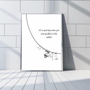 Può includere: Stampa incorniciata con sfondo bianco e disegno a tratto nero. L'opera presenta una linea curva con disegni di bikini appesi. Il testo recita: "It's a good day when you change Bikinis Like outfits."