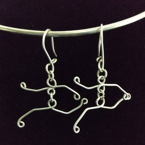May include: A pair of silver wire earrings shaped like abstract figures. The earrings are hanging from a silver hook.