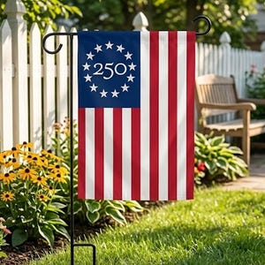 May include: A garden flag featuring a design reminiscent of the American flag, with red and white stripes and a blue field with white stars and the number 250. The flag is displayed on a black metal stand in a garden setting.