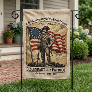 Op de afbeelding: Een beige tuinvaandel met een vintage illustratie van een koloniale soldaat en de Amerikaanse vlag. Tekst luidt "250th Anniversary of the United States - 1776-2026" en "Descendant of a Patriot". De vlag staat op een zwarte metalen standaard.
