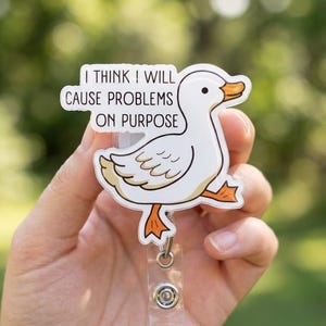 May include: A white duck badge reel with orange beak and feet, and the text "I THINK I WILL CAUSE PROBLEMS ON PURPOSE". The badge reel has a clear plastic strap and a metal clip.