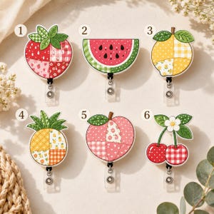 May include: Six fruit-themed badge reels numbered one to six. Designs include a strawberry, watermelon slice, lemon, pineapple, peach, and cherries. Each features a patchwork pattern with various red, yellow, pink, and green colours.