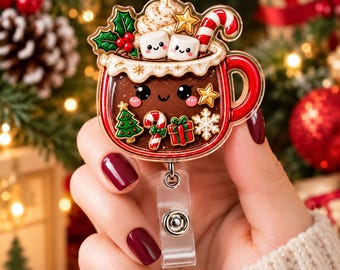 Op de afbeelding: Een badgehouder van doorzichtig acryl in de vorm van een mok warme chocolademelk, met slagroom, twee lachende marshmallows en een zuurstok. De mok is versierd met een kerstboom, een zuurstok, een cadeautje en een sneeuwvlokje.