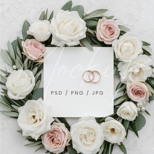 Peut inclure: Image sur le thème du mariage avec une couronne florale de roses blanches et roses, de feuilles vertes et de perles. Deux alliances dorées reposent sur un carré blanc avec le texte "PSD / PNG / JPG". Fond en dentelle blanche.