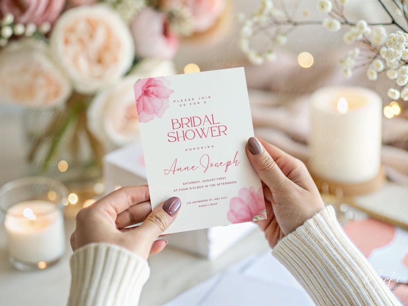 May include: A pink and white bridal shower invitation with watercolor flowers and the text "Please join us for a Bridal Shower Honoring Anne Joseph Saturday, August First at Four O'Clock in the Afternoon The Residence of Amy Smith 123 Example Way, Any City, Any State 12345"