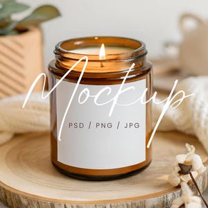May include: A brown glass candle jar with a white label that says "Mockup PSD / PNG / JPG". The candle is lit and the jar is sitting on a wooden slice.