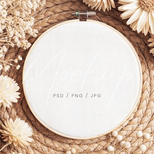 May include: A blank white cross-stitch hoop with a wooden frame, surrounded by dried flowers and set against a woven background. The text "PSD / PNG / JPG" is printed on the white fabric.