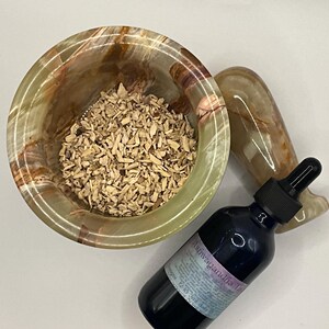 Puede incluir: Un mortero de &oacute;nix verde y marr&oacute;n lleno de virutas de madera, un mortero a juego y una botella azul oscuro con un cuentagotas. La botella tiene una etiqueta que dice "Tintura de Ashwagandha".