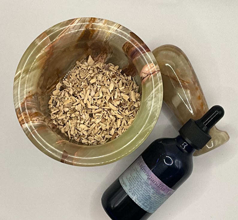 Puede incluir: Un mortero de &oacute;nix verde y marr&oacute;n lleno de virutas de madera, un mortero a juego y una botella azul oscuro con un cuentagotas. La botella tiene una etiqueta que dice "Tintura de Ashwagandha".