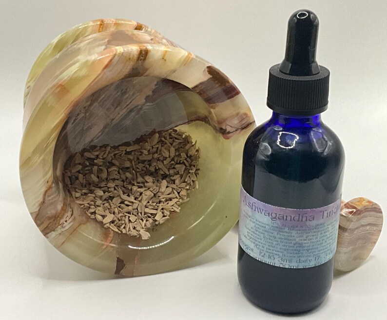 Puede incluir: Una botella de vidrio azul de tintura de Ashwagandha con un cuentagotas negro se encuentra junto a un cuenco de &oacute;nix tallado lleno de virutas de madera. Tambi&eacute;n hay un peque&ntilde;o coraz&oacute;n de &oacute;nix.