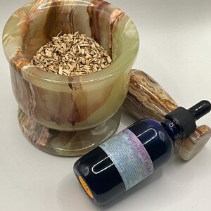 Puede incluir: Un juego de mortero y maja de &oacute;nix verde, marr&oacute;n y beige lleno de virutas de madera, junto a una botella de vidrio azul con un cuentagotas negro. La botella tiene una etiqueta con texto. La maja es del mismo material de &oacute;nix.