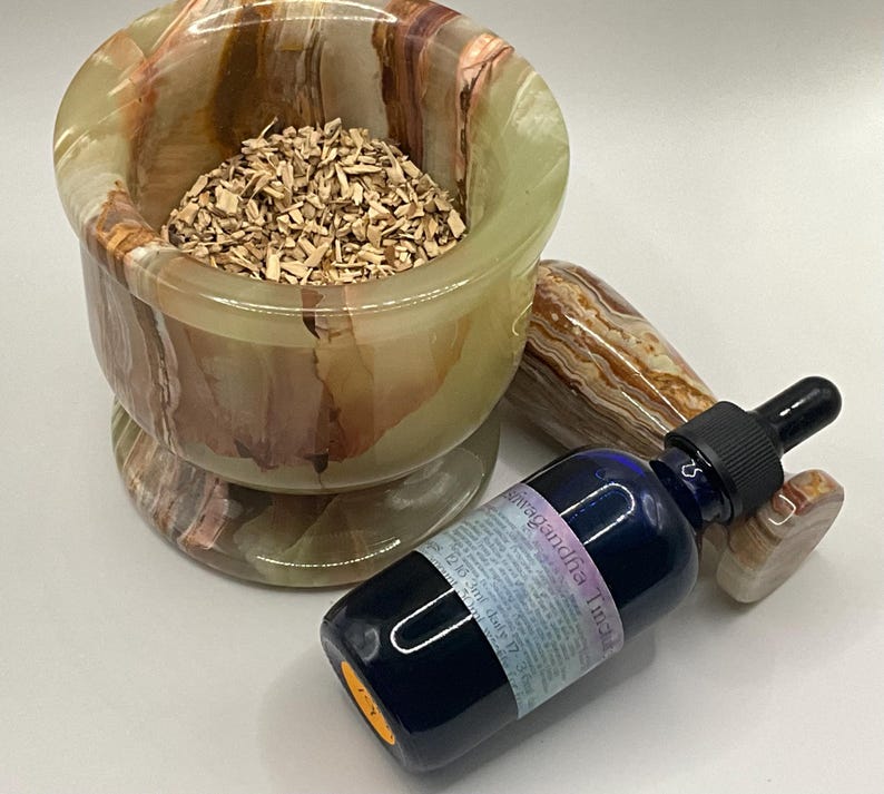 Puede incluir: Un juego de mortero y maja de &oacute;nix verde, marr&oacute;n y beige lleno de virutas de madera, junto a una botella de vidrio azul con un cuentagotas negro. La botella tiene una etiqueta con texto. La maja es del mismo material de &oacute;nix.