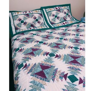 May include: A quilted bedspread and two pillow shams featuring a repeating geometric pattern in shades of white, teal, purple, and green. The quilt has a white background with a teal border and a detailed design.